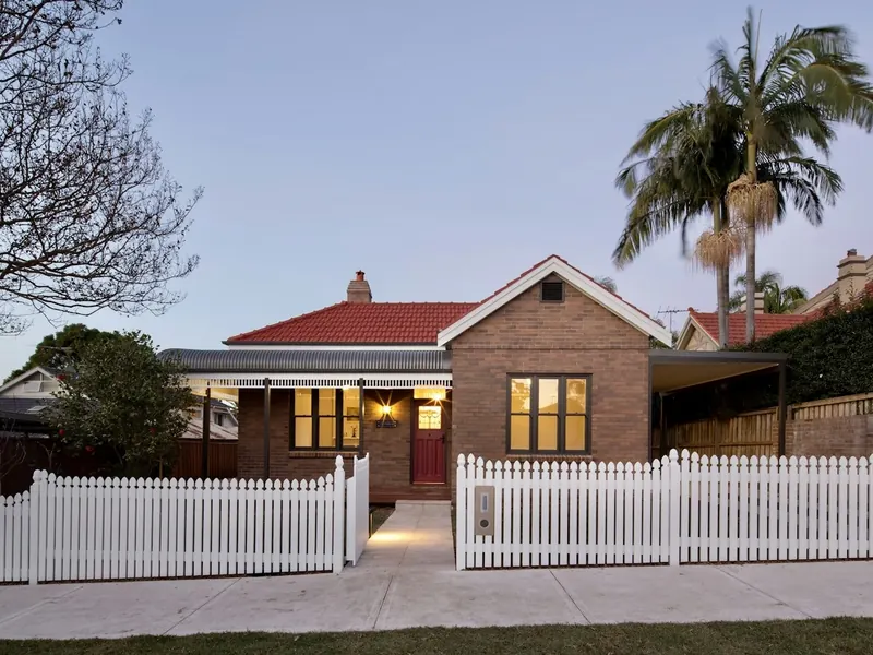 White picket fence in front of a brick home